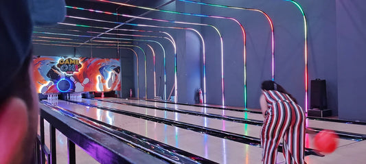 A young woman bowls in a brightly lit alley with colorful neon lights.