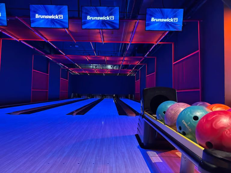 A bowling alley with blue and pink lighting, showing bowling balls on a rack.