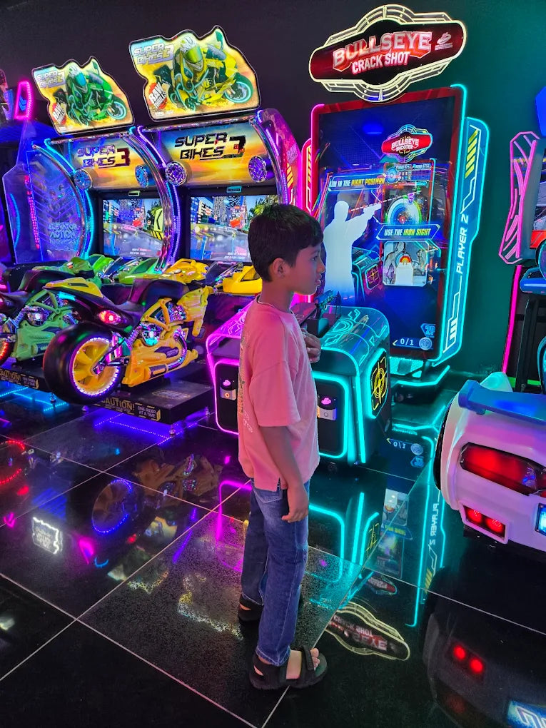 A young boy stands in an arcade, looking at a "Bullseye Crack Shot" game.