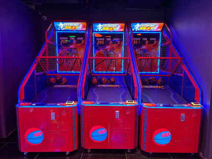 Three red arcade basketball shooting games with blue neon lights, set up side-by-side in an entertainment venue.