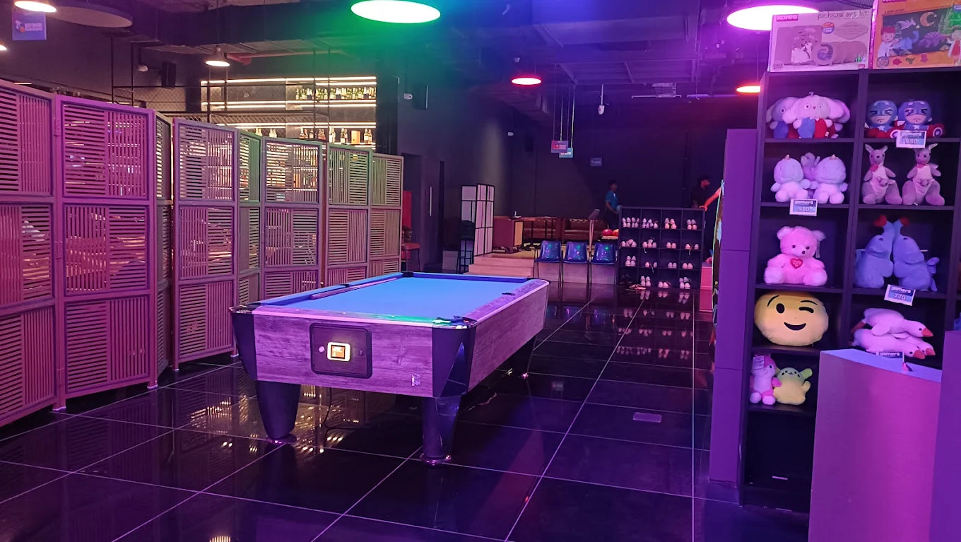 A pool table and shelves of plush toys in a dimly lit entertainment venue.