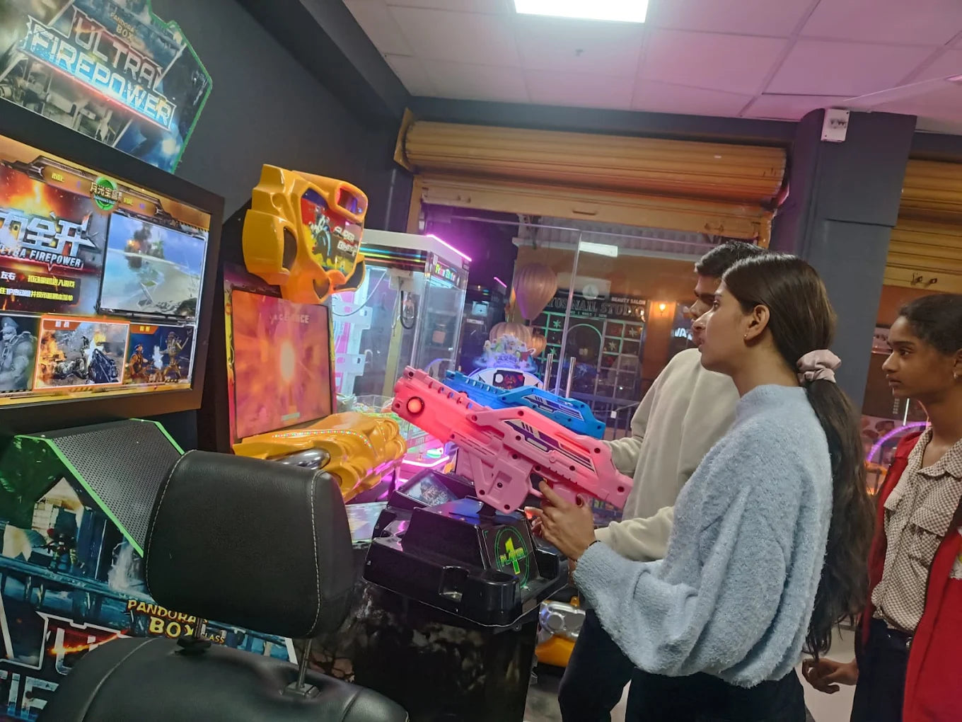 Young people play a shooting game at an arcade, holding colorful toy guns.