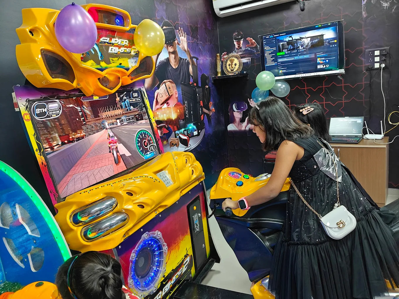 Two young girls play a motorcycle racing arcade game in a colorful, VR-themed arcade.