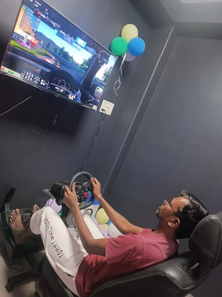 A young man plays a racing video game using a steering wheel and pedals while sitting in a gaming chair.