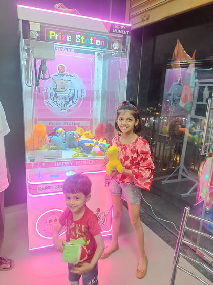 Two children stand in front of a brightly lit prize machine, one holding a yellow stuffed toy and the other a green one.