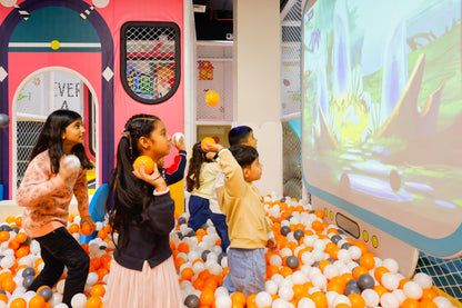 Children playing in a ball pit with colorful walls and a large screen displaying a cartoon scene.