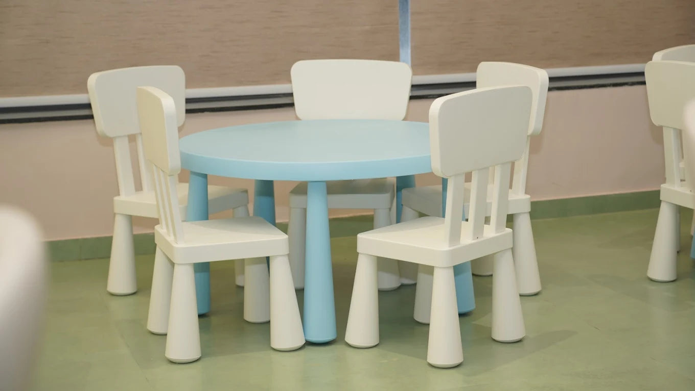 A round, light blue table with white chairs for children in a classroom.