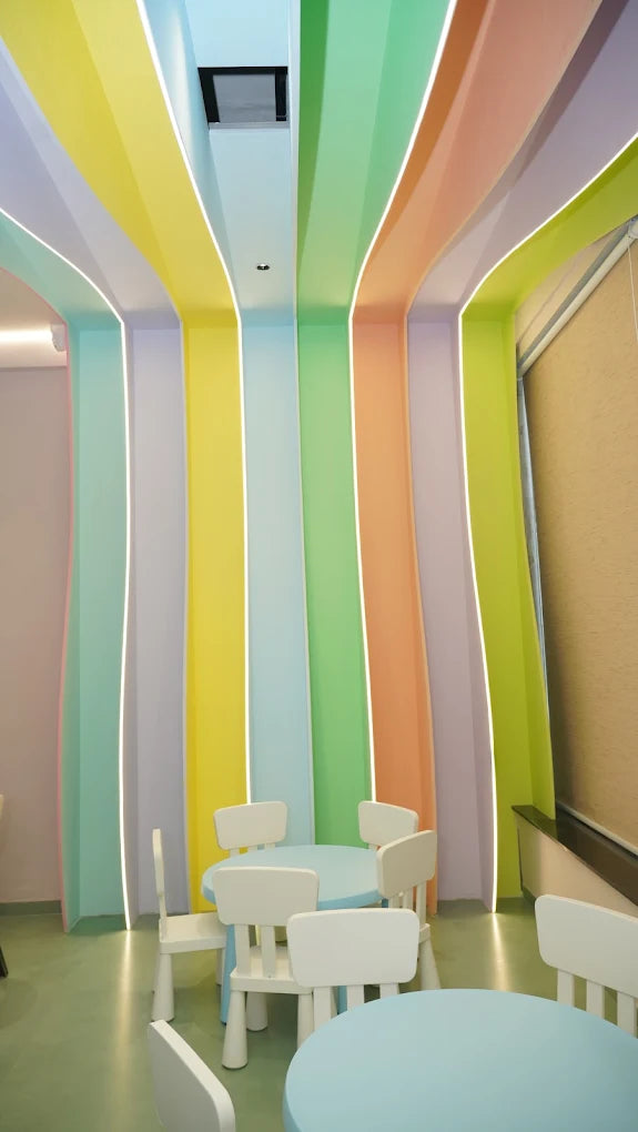 A colorful room with pastel-colored walls and ceiling, featuring small tables and chairs for children.