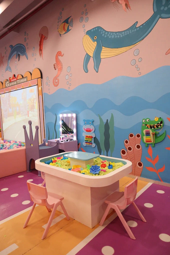 A children's play area with a sand table, ball pit, and ocean-themed wall art.