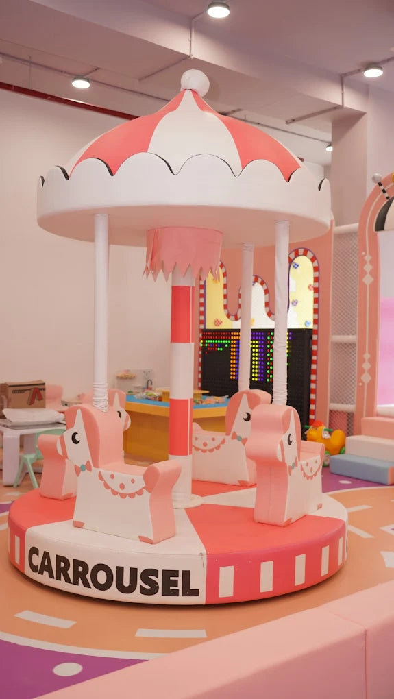 A pink and white carousel with horse-shaped seats in a children's play area.