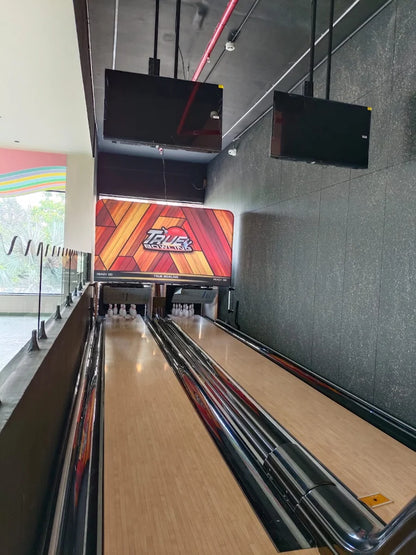 A bowling alley with two lanes, pins set up, and screens hanging overhead.
