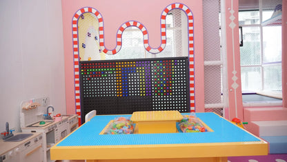 A colorful playroom with a large building block table and a pegboard activity wall.