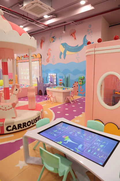 A colorful indoor playground with a carousel, interactive table, and ocean-themed murals for children.