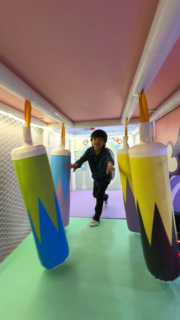 A young boy runs through a colorful indoor playground with hanging inflatable obstacles.