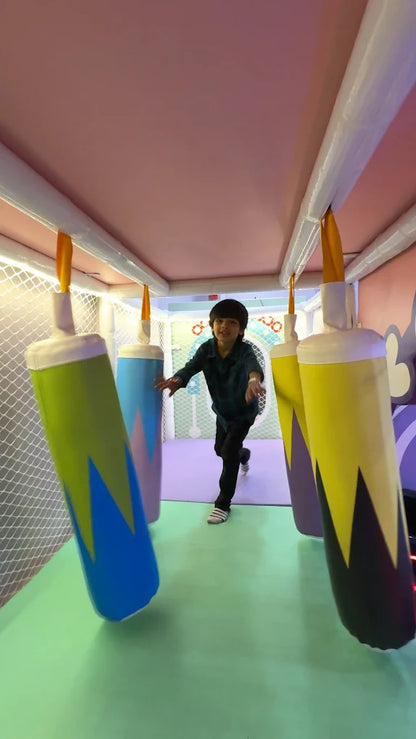 A young boy runs through a colorful indoor playground with hanging inflatable obstacles.