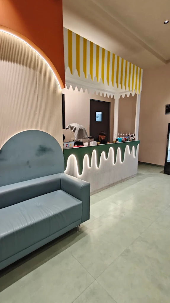 A young man works behind a counter in a brightly decorated shop with a blue sofa in the foreground.