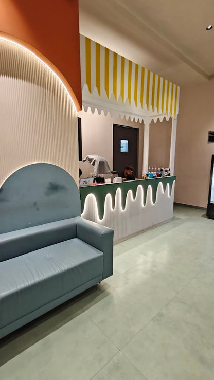 A young man works behind a counter in a brightly decorated shop with a blue sofa in the foreground.