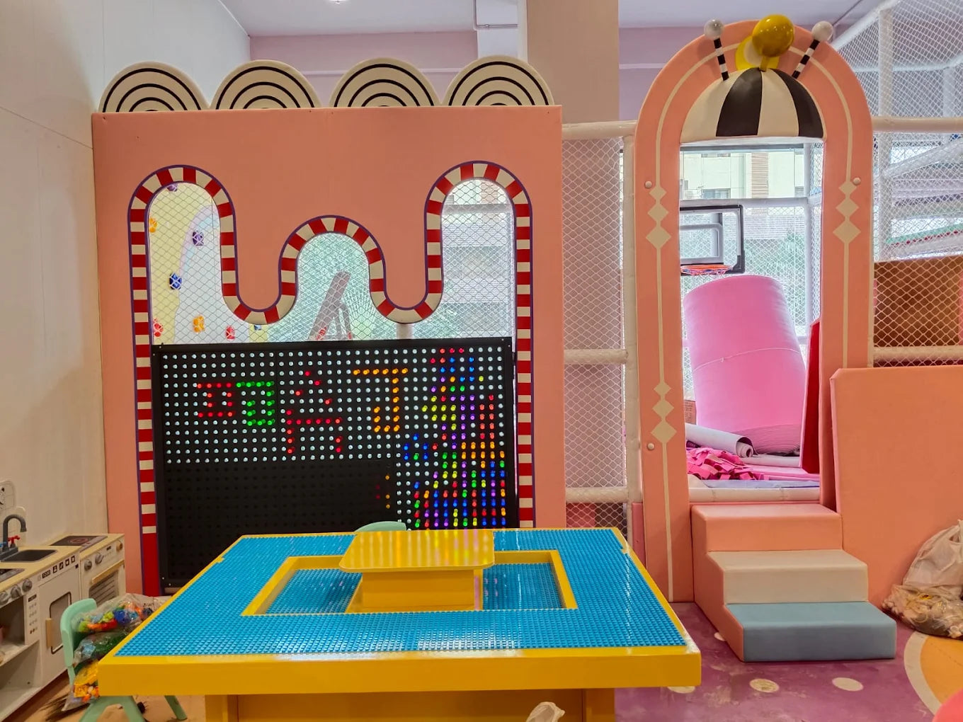 A colorful indoor playground with a large light-up board and a building block table for children.