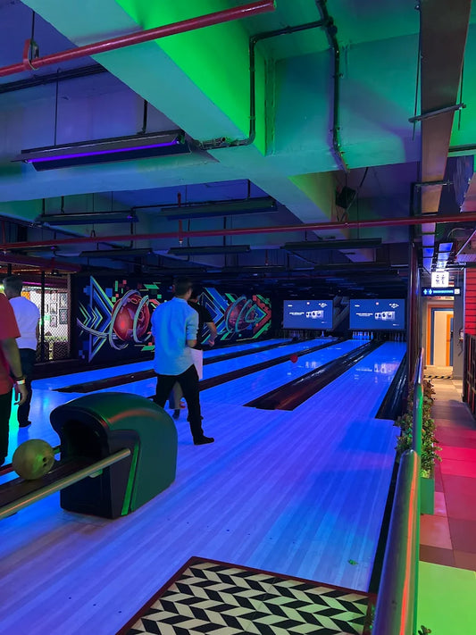 People bowling in a dimly lit alley with neon blue and green lights.