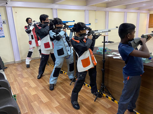 Young people practice shooting at a range, aiming rifles at targets.