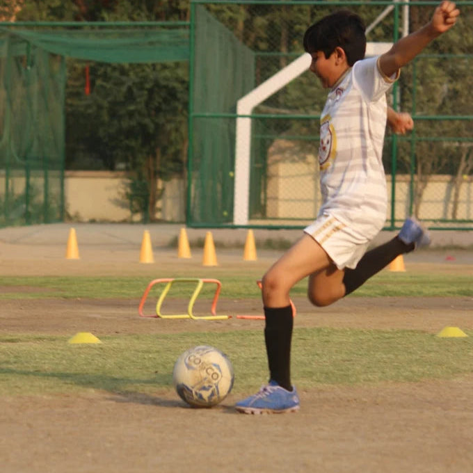 Child playing soccer on a field with cones and a goal in the background