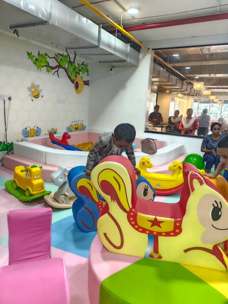 Children play in a colorful indoor playground with ball pit and animal-themed rides.