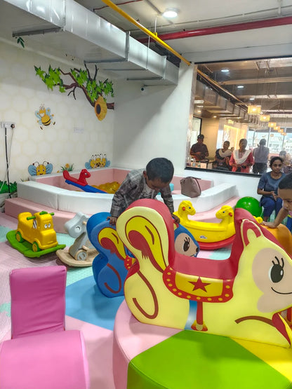 Children play in a colorful indoor playground with ball pit and animal-themed rides.
