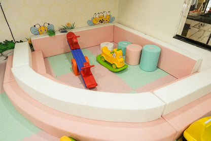 A soft play area for toddlers with a seesaw, ride-on toy, and colorful blocks.