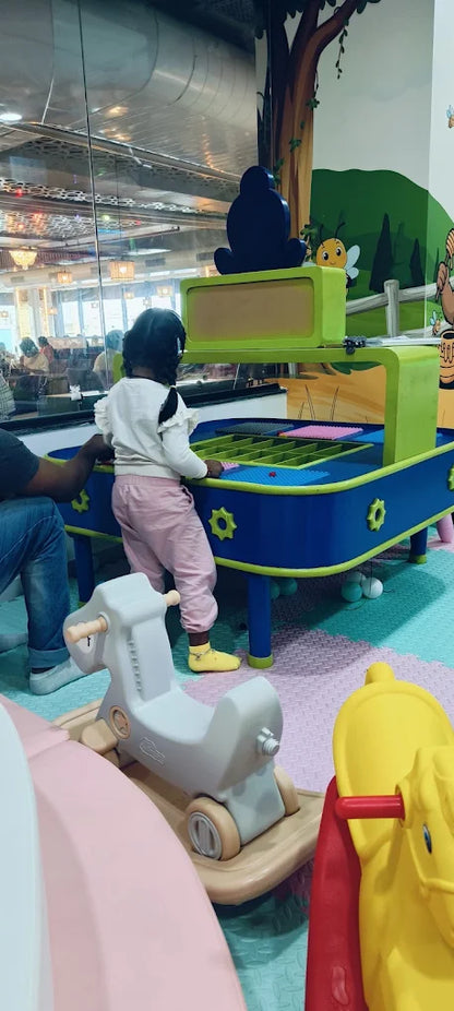 A young child plays at a colorful activity table in a bright indoor play area.