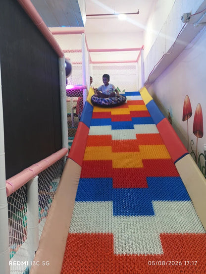 A young boy slides down a colorful indoor playground slide on a tube.