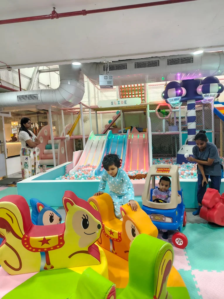 Children play in a colorful indoor playground with slides and ball pits.