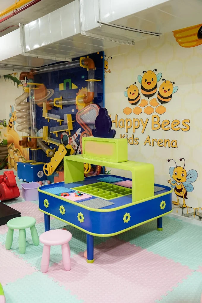 A colorful kids' play area with a busy bee theme, featuring a large activity table and a ball maze.