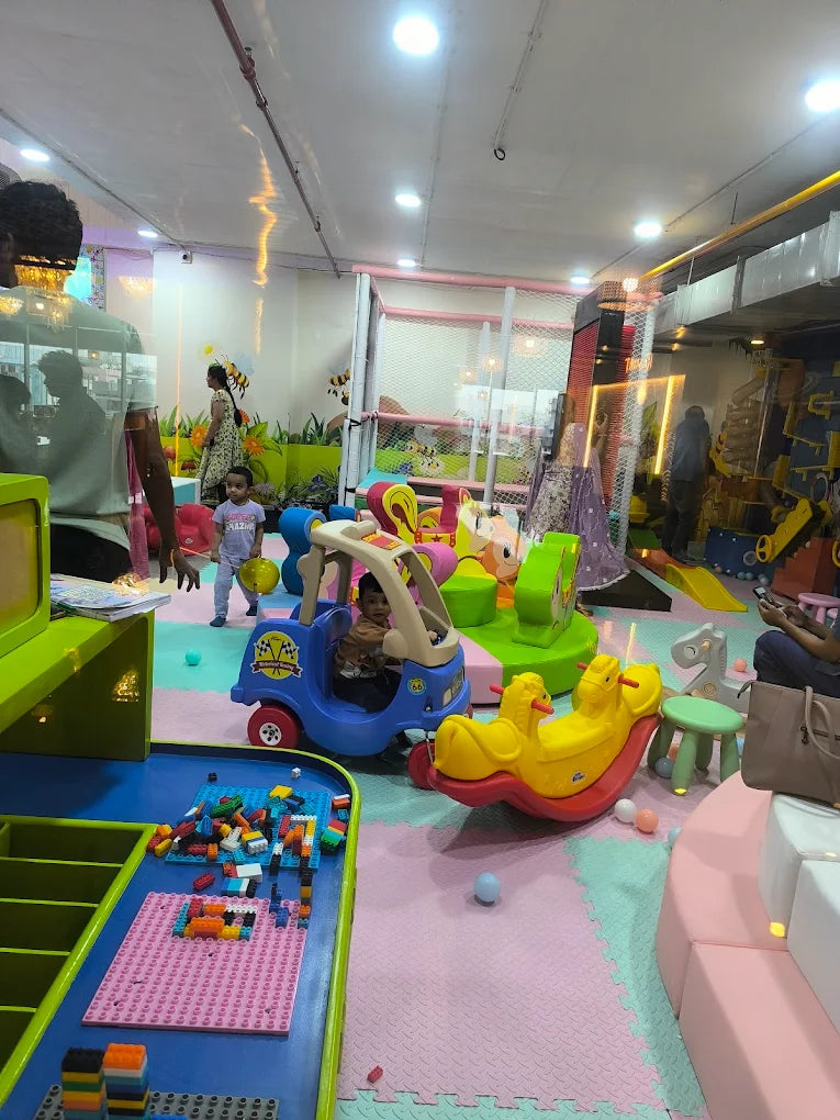 Children play in a colorful indoor playground with toys and soft flooring.