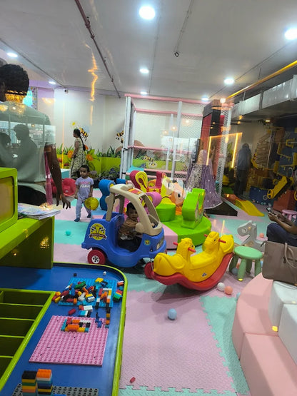 Children play in a colorful indoor playground with toys and soft flooring.