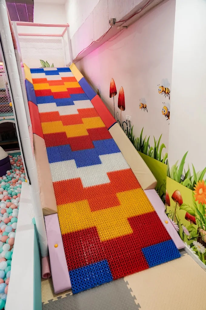A colorful slide in a children's play area leads to a ball pit.