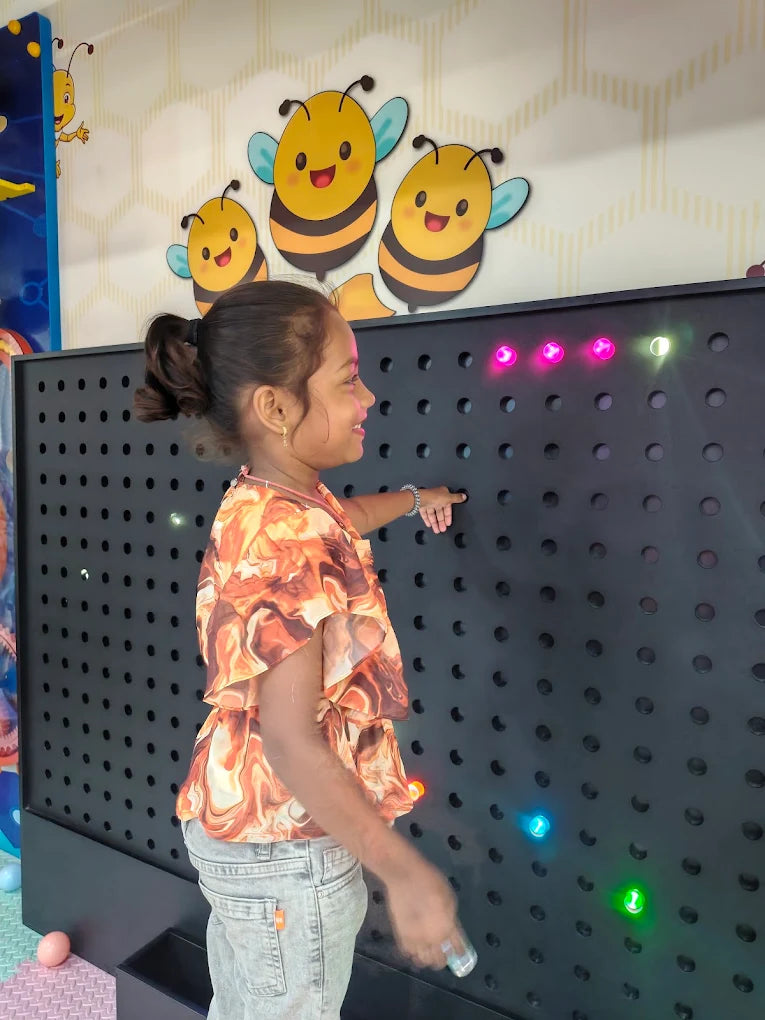 A young girl plays with a light-up wall in a colorful room decorated with bees.