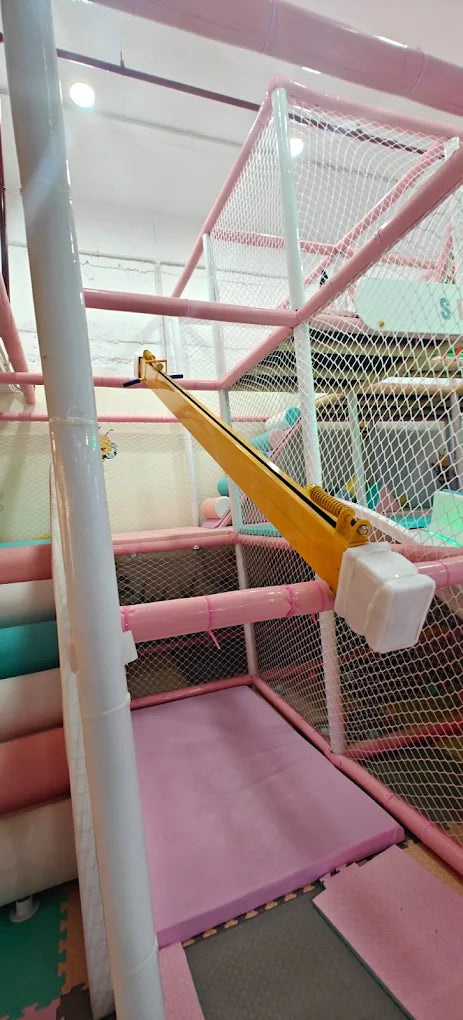 A yellow crane toy in a pink and white indoor playground for children.