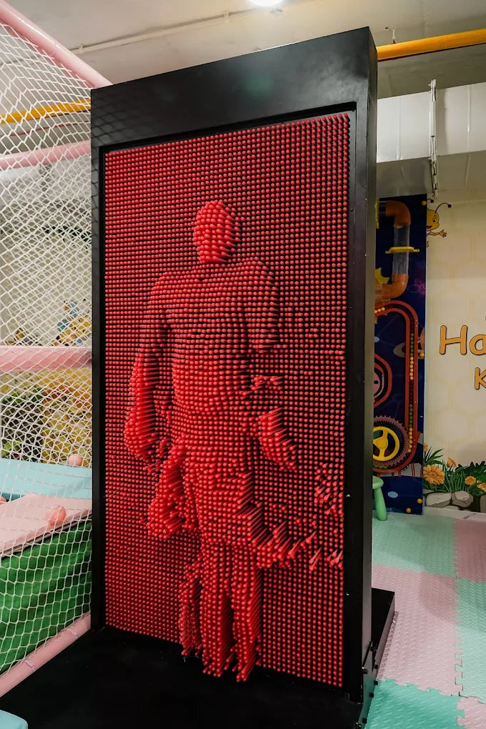 A person's silhouette is imprinted on a red pin art toy in a children's play area.