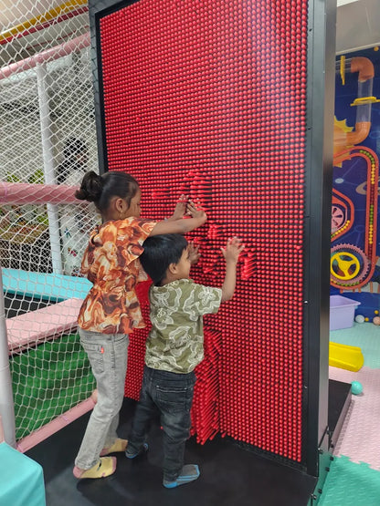 Two young children play with a large red pin art toy in an indoor play area.