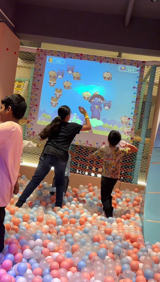 Children play an interactive game projected onto a screen, surrounded by a ball pit.