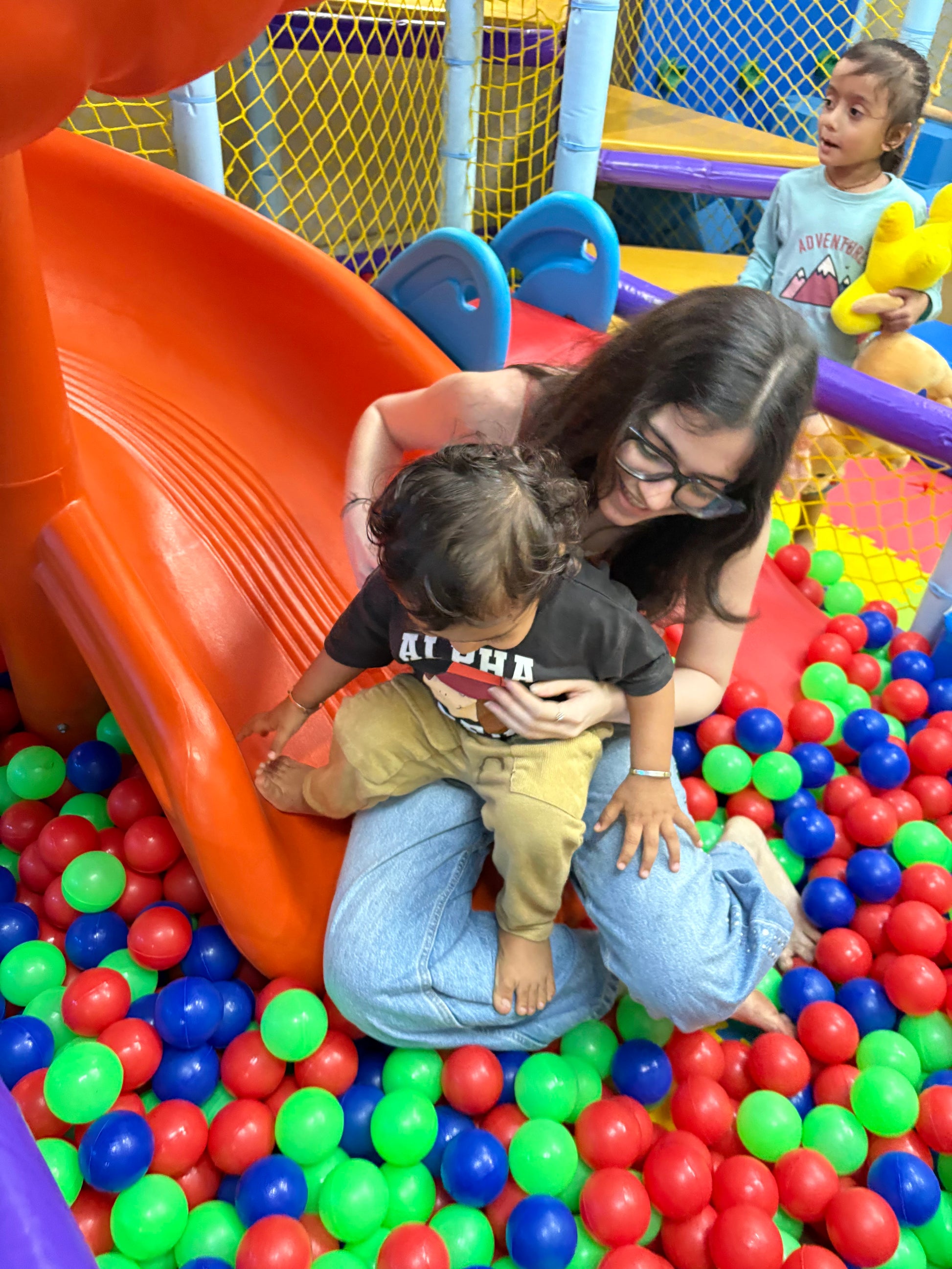 A young child and an adult play in a ball pit with a slide.