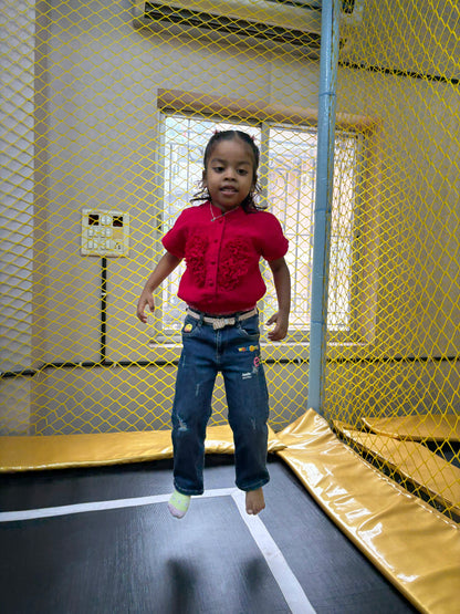 A young girl jumps on a trampoline inside a play area with yellow netting.