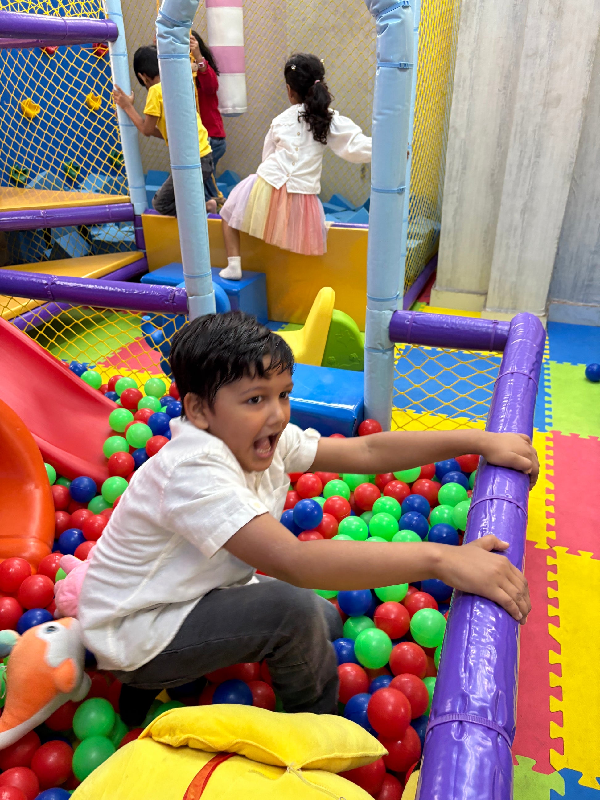A young boy excitedly plays in a ball pit at an indoor playground.