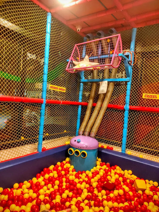 A ball pit with red and yellow balls, a star toy, and tubes leading to a basket.