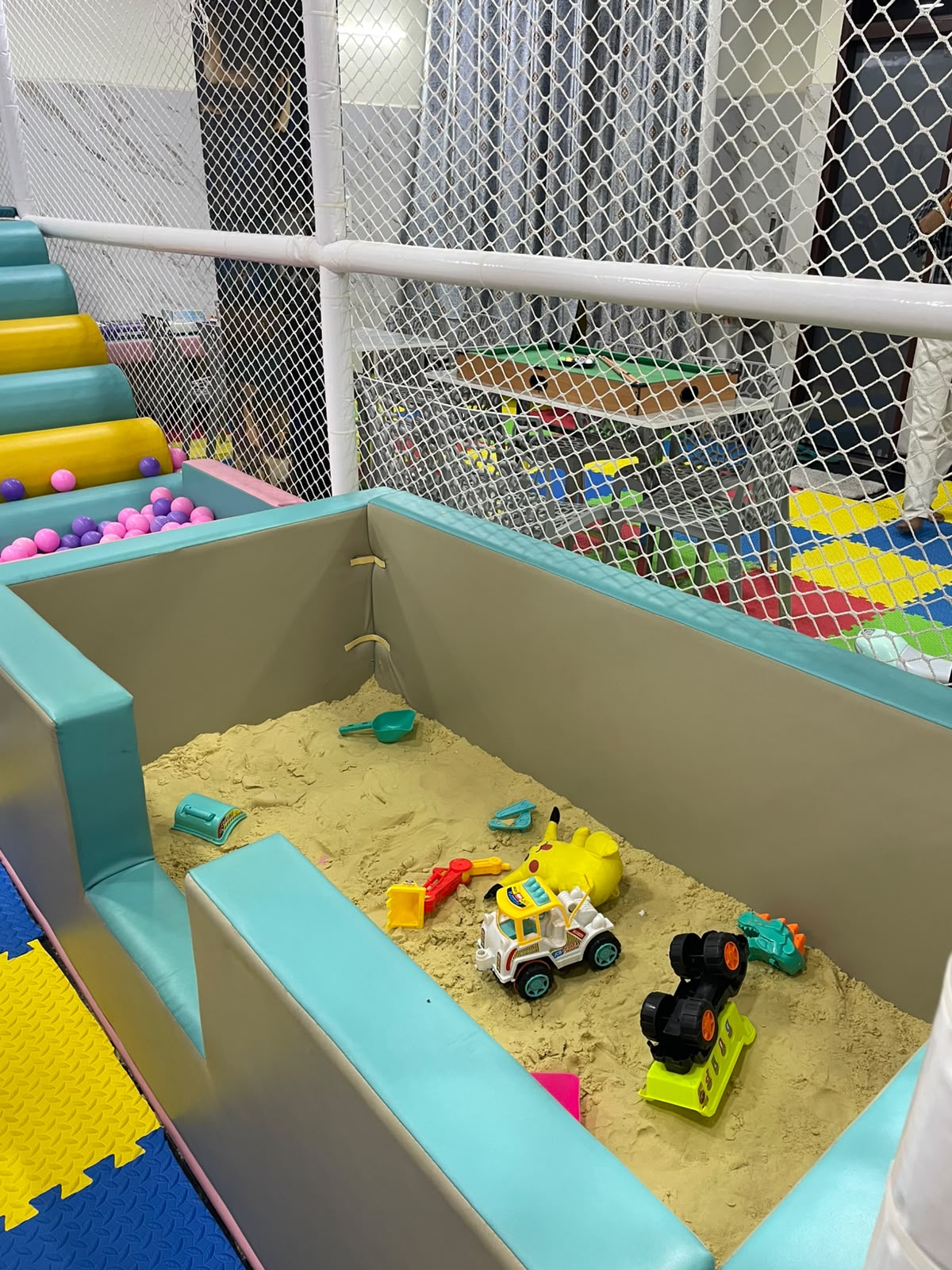 A sandpit with toys and a ball pit in a children's play area.