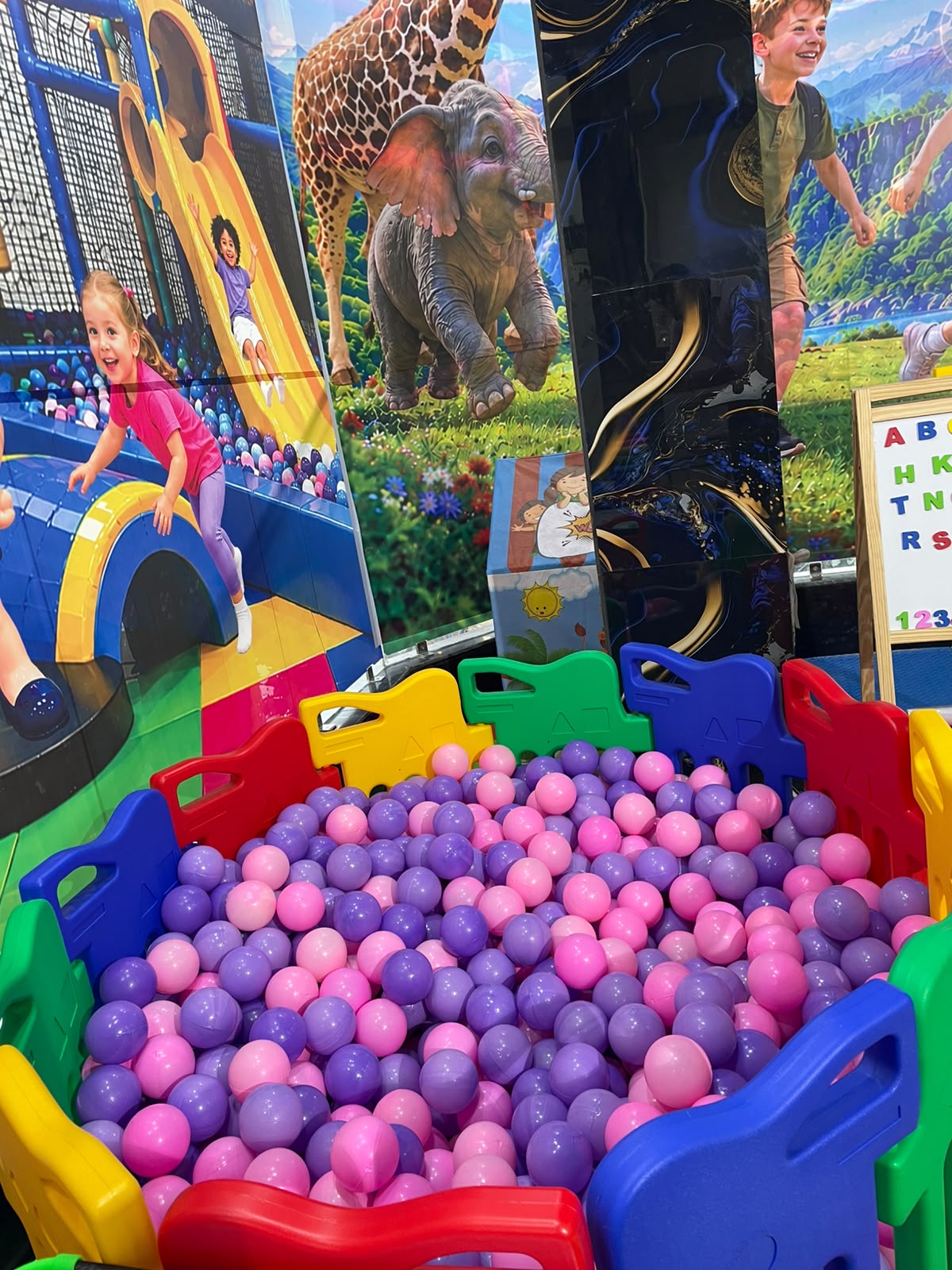 Children play in a ball pit with a jungle-themed backdrop.