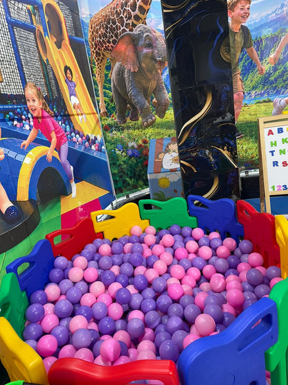 Children play in a ball pit with a jungle-themed backdrop.