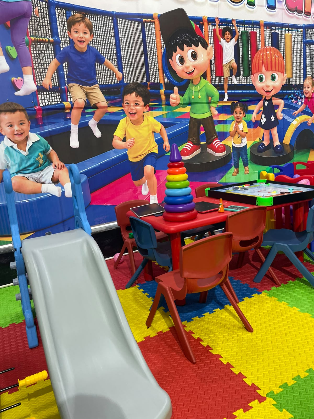 Children play in a colorful indoor playground with slides and tables.