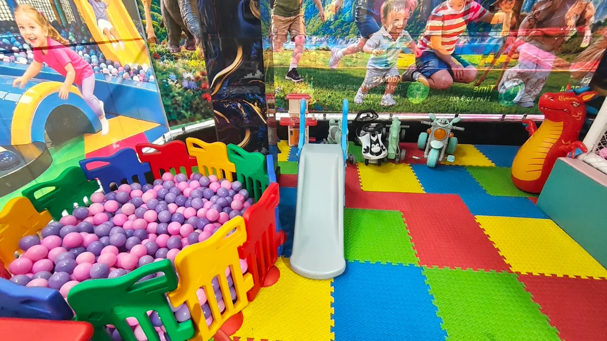 A young girl plays in a ball pit at an indoor playground with a slide and toy motorcycles.