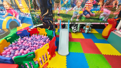 A young girl plays in a ball pit at an indoor playground with a slide and toy motorcycles.